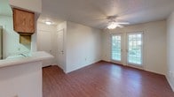 This single-floor residence offers a practical and comfortable layout designed for everyday living. The open-concept living area is finished with warm hardwood-style flooring that flows throughout the main spaces, creating a cohesive and inviting atmosphere. A ceiling fan provides both lighting and air circulation, while double French doors along one wall allow natural light to filter in and provide access to the outdoors.

The kitchen is efficiently arranged and opens to the living area via a peninsula-style breakfast bar, making the space feel connected and sociable. It is equipped with white appliances including a refrigerator, electric range, and microwave, complemented by light wood cabinetry and under-cabinet storage. The layout maximizes functionality within the available footprint.

The bedroom is carpeted for comfort and features its own ceiling fan with light fixture, along with a window fitted with blinds that allows natural light while maintaining privacy. The textured ceiling is consistent throughout the residence, adding subtle visual depth.

The bathroom is well-appointed with hardwood-style flooring, a full soaking tub and shower combination surrounded by neutral large-format tile, a toilet, and a vanity with an integrated sink. A wall-mounted ventilation unit ensures proper airflow. Overall, the space presents a clean, no-frills design that prioritizes functionality and livability.