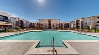 Located at 5614 Thompson Mill Rd in Hoschton, Georgia, this outdoor amenity area serves as the centerpiece of a modern residential community. The space is dominated by a generously sized, resort-style swimming pool with crystal-clear water, flanked by a wide, decorative concrete sundeck. The pool area is thoughtfully designed for recreation and relaxation, featuring multiple lounge chairs and seating arrangements positioned to take full advantage of the open sky and abundant natural sunlight. A dedicated shallow entry area and clearly marked depth indicators reflect careful attention to safety and usability. Surrounding the pool, the courtyard extends into a well-landscaped outdoor seating zone, complete with bistro-style tables and chairs nestled among neatly maintained shrubs, mulched garden beds, and young trees that add greenery and shade. A covered pergola structure provides an additional shaded retreat. The entire amenity space is enclosed by sleek iron fencing and is framed on multiple sides by contemporary multi-story residential buildings finished in neutral tones with accented balconies, large windows, and modern architectural detailing. The overall ambiance is open, bright, and community-oriented, offering residents an inviting outdoor environment well-suited for both active recreation and leisurely gatherings.