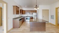 Located in Otsego, MN, this two-bedroom, two-bathroom single-floor residence offers a well-designed layout that balances comfort and functionality. The open-concept kitchen and living area serves as the heart of the home, featuring rich warm-toned cabinetry, granite countertops, a central island, and a full suite of stainless steel appliances including a dishwasher, range, and microwave. A decorative pendant chandelier adds a refined touch above the kitchen island, while light wood-style flooring flows throughout the main living areas. The living room is bathed in natural light and opens directly to a private balcony through sliding glass doors, offering pleasant outdoor views. A ceiling fan keeps the space comfortable year-round. Both bedrooms are carpeted and filled with natural light from generously sized windows that overlook the surrounding neighborhood. The spacious primary bedroom features a tray ceiling and a walk-in closet with wire shelving. Each bathroom is finished with warm wood cabinetry, white countertops, and framed mirrors with contemporary lighting. A dedicated laundry room houses a full-size washer and dryer, adding everyday convenience. Additional storage and a utility room round out this thoughtfully arranged home.