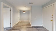 This single-floor space presents a cohesive, modern aesthetic built around a neutral color palette of soft gray-blue walls, crisp white trim, and light wood-look luxury vinyl plank flooring that runs consistently throughout. The open layout is anchored by a central corridor fitted with a stylish drum pendant light, creating a welcoming transition between rooms. Multiple doorways branch off this hallway, providing clear separation between living areas.

The bedrooms are generously proportioned, each featuring ceiling fans with integrated lighting and windows fitted with horizontal blinds that allow for controlled natural light. The light tones of the walls and flooring give these rooms an airy, bright quality.

The kitchen is outfitted with white shaker-style cabinetry, gray countertops, a stainless steel undermount sink, a stainless steel dishwasher, and a refrigerator. The clean lines and neutral finishes create a functional and visually consistent cooking space that connects smoothly to the rest of the unit.

The bathroom includes a full-size soaking tub with a shower, surrounded by white square tile from tub to ceiling and chrome fixtures. The overall ambiance of the space is clean, contemporary, and move-in ready.