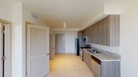 This single-floor space presents a thoughtfully designed layout with modern finishes and a cohesive neutral palette throughout. The kitchen serves as a standout feature, outfitted with dark wood-grain cabinetry extending from counter to ceiling, granite countertops, a classic white subway tile backsplash, and stainless steel appliances including a range, built-in microwave, dishwasher, and refrigerator. A double-basin sink sits beneath a wall of upper cabinets, maximizing storage. Light tile flooring runs throughout the unit, lending a clean and consistent look. Natural light flows in from a sliding glass door adjacent to the kitchen, offering access to a balcony with outdoor views. The bedroom is a bright, well-proportioned space with a ceiling fan, large window overlooking the surrounding area, and the same light tile flooring. The bathroom is designed with accessibility in mind, featuring grab bars, a roll-in shower with handheld fixture, a sleek vanity with wood-toned cabinetry, a wide mirror, and tile flooring. A louvered closet door adds a classic touch near the entryway. Overall, the space combines functional design with contemporary aesthetics, creating a clean and comfortable living environment.