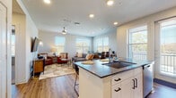 This single-floor residence is designed with a modern, open-concept layout that integrates the kitchen, dining, and living areas into one cohesive, light-filled space. The kitchen is equipped with stainless steel appliances, white shaker-style cabinetry, dark granite countertops, and a central island with bar seating and an undermount sink — functioning as both a practical workspace and a social hub. Wood-style plank flooring extends throughout the main living area, complementing the neutral palette and recessed lighting overhead. Multiple windows fitted with horizontal blinds invite ample natural light and outdoor views into the living room, which also features a ceiling fan.

The primary bedroom is generously sized with plush carpet flooring and direct access to an en-suite bathroom. The bathroom includes a dual-sink vanity with dark granite countertops, white cabinetry, a bathtub with shower, wood-style flooring, and an adjacent walk-in closet with built-in shelving. A second bedroom also features carpet, a ceiling fan, and a large window. An additional bathroom nearby offers a glass-enclosed shower and access to a walk-in closet, rounding out a well-organized and functional floor plan.