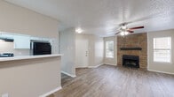 This single-story 1-bedroom, 1-bathroom unit offers a thoughtfully designed layout across a compact and efficient floor plan. The combined kitchen and living area serves as the heart of the space, featuring light wood-look tile flooring, neutral wall tones, and a textured ceiling throughout. A striking floor-to-ceiling stone fireplace with a dark wood mantel anchors the living room, adding warmth and character. A ceiling fan with integrated lighting keeps the space comfortable, while multiple windows dressed with horizontal blinds invite natural light. A private exterior door in the living area provides convenient access to the outdoors.

The kitchen is separated by a raised breakfast bar with white quartz-style countertops, offering a practical pass-through to the living space. White cabinetry, a black refrigerator, and built-in open shelving complete the kitchen area. The bedroom is carpeted for comfort and includes a closet and a window with natural light. The full bathroom features a tub-shower combination with white tile surround, white cabinetry with ample storage overhead, and wood-look flooring that ties in with the rest of the unit. A hallway connects the private spaces, completing this functional and cozy single-floor layout.