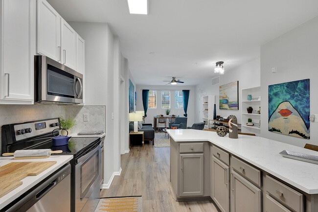 Modern open-plan kitchen and living area with sleek cabinetry, stainless steel appliances, and vibrant decor, offering a stylish and inviting ambiance. - Avia Lowry