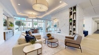 Located at 111 Green St SE in Gainesville, Georgia, this single-floor amenity space exemplifies contemporary design with a refined, upscale aesthetic throughout. The expansive lounge area serves as the centerpiece, featuring tray ceilings with recessed lighting and oversized drum pendant fixtures in warm gold tones. A dramatic floor-to-ceiling marble accent wall anchors the room, complemented by light hardwood-style flooring and large floor-to-ceiling windows that flood the space with abundant natural light and offer views of the surrounding streetscape. The lounge is furnished with generous sectional sofas, accent chairs, and tiered round coffee tables, creating an inviting and versatile gathering environment. Built-in shelving units provide both functional storage and curated display space. An adjacent dining and bar area with counter-height seating and a wall-mounted television extends the entertaining capabilities of the space. Glass-enclosed conference rooms, identifiable by sleek signage, offer intimate meeting settings complete with round tables, upholstered chairs, statement chandeliers, and wall-mounted displays. The fitness center, also accessed through glass walls, is well-equipped with cardio and strength training equipment, tray ceilings, ceiling fans, and ample natural light, rounding out this thoughtfully designed, multifunctional space.