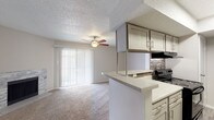 Located at 1701 Victoria Station Dr in Victoria, Texas, this single-floor unit offers a well-designed, functional layout that balances comfort and practicality. The open-concept living and dining area is anchored by a striking stone-surround fireplace, plush wall-to-wall carpeting, and a ceiling fan overhead. Large sliding glass doors dressed with vertical blinds invite natural light and provide outdoor access, enhancing the sense of openness throughout the main living space. The galley-style kitchen is thoughtfully appointed with gray shaker-style cabinetry, light quartz countertops, a mosaic tile backsplash, and black appliances including a range, refrigerator, and dishwasher. A peninsula counter connects the kitchen to the living area, making it ideal for casual dining or entertaining. Wood-look flooring runs through the kitchen and entry areas, offering a clean contrast to the carpeted rooms. The bedroom is generously sized with a ceiling fan, a windowed wall for natural light, and an impressive amount of closet storage, including walk-in options. The bathroom features a quartz vanity, gray cabinetry, a large mirror, and a tiled shower-tub combination. A textured ceiling is consistent throughout the unit, adding a classic residential character to the overall aesthetic.
