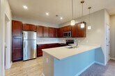 Located at 16636 Chicago Plaza in Omaha, Nebraska, this well-appointed one-bedroom, one-bathroom residence offers a thoughtfully designed single-floor layout. The kitchen is a standout feature, showcasing rich dark-wood cabinetry extending to the ceiling, light quartz countertops, stainless steel appliances including a refrigerator, range, and microwave, and a spacious peninsula with an integrated sink illuminated by stylish pendant lighting. Light wood-look flooring anchors the kitchen and transitions seamlessly into adjoining areas. The living room is bright and welcoming, featuring plush carpet, a bay-style window arrangement with white shutters, a glass-front fireplace as a central focal point, and direct access to an outdoor balcony through a glass-paned door. The generously sized bedroom offers comfortable carpet flooring, a ceiling fan, and a large window that fills the room with natural light, while a walk-in closet with built-in shelving provides ample storage. The bathroom includes a full tub and shower combination with wood-look tile flooring. A dedicated in-unit laundry room with a washer and dryer adds everyday convenience. A staircase connects to the entry level, completing this functional and modern layout.