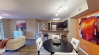 This well-appointed single-floor residence showcases a bold and cohesive interior design anchored by warm orange accent walls and rich, dark wood finishes throughout. The open-concept living area is generously sized, featuring wood-style flooring, a ceiling fan, and a striking accent wall adorned with decorative wall panels. Sliding glass doors lead to a private balcony, allowing natural light to fill the space and offering outdoor views. The adjacent kitchen is fully equipped with stainless steel appliances, dark cabinetry, granite-style countertops, a double sink, and a breakfast bar that connects seamlessly to the dining area. The dining space accommodates a round table with seating and benefits from track lighting overhead. The primary bedroom is a standout feature, with a vibrant orange accent wall, plush carpeting, a ceiling fan, and a large window. A second bedroom offers similar comfort with neutral tones, carpet flooring, natural light, and closet storage. Both bathrooms are finished with dark vanity cabinetry, granite-style countertops, and tile flooring. One bathroom includes a shower-tub combination. The overall ambiance is energetic and stylish, blending warm tones with functional, well-designed living spaces.