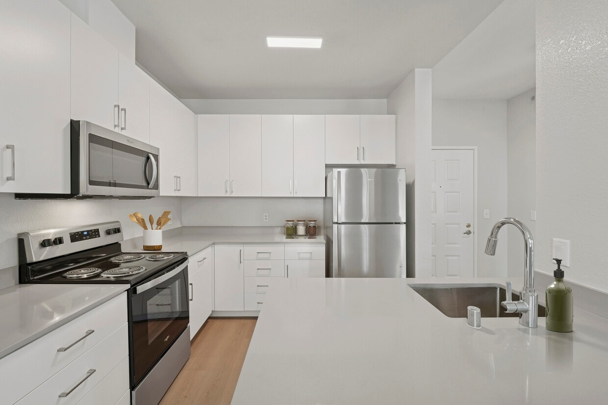 Renovated Package I kitchen with white cabinetry, grey quartz countertops, stainless steel appliances, and hard surface flooring - Avalon Fremont