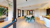 Located in Philadelphia's vibrant Northern Liberties neighborhood, this thoughtfully designed amenity floor at 23 W Girard Ave offers residents a comprehensive suite of shared spaces spanning an expansive footprint. The centerpiece is a well-appointed fitness center featuring cardio machines, a rowing machine, and a weight bench, all beneath a striking ceiling with circular wood-slatted panels and bold ring-shaped pendant lighting that lend the room a boutique gym aesthetic. Adjacent is a dedicated yoga and barre studio, outfitted with light hardwood flooring, a wall-mounted barre, a large illuminated round mirror, and direct access to the outdoor terrace — ideal for focused movement and wellness routines. A sophisticated lounge area serves as a social hub, highlighted by deep navy accent walls adorned with large arched floral murals, plush olive-green banquette seating, and modern white lounge chairs set atop light wood flooring. A compact, private meeting room features a round marble-top table and a wall-mounted display, perfect for focused work or small gatherings. The floor also connects seamlessly to a generous outdoor deck fitted with composite decking, black steel railings, dining and lounge furniture, and open views of the surrounding Philadelphia skyline and rooftops.
