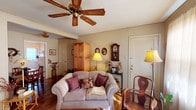 This single-floor, one-bedroom, one-bathroom residence offers a warm and inviting atmosphere with a distinctly vintage character throughout. The living room serves as a welcoming focal point, featuring hardwood flooring, crown molding, a wood-bladed ceiling fan, and large sheer-draped windows that allow natural light to filter softly into the space. A comfortable seating arrangement and classic decorative accents give the room a cozy, lived-in feel. Adjacent to the living area, a dedicated dining nook accommodates a wooden table and chairs, accented by wall art and a decorative wreath, creating an intimate space for meals. The kitchen is efficiently laid out with white cabinetry offering open shelving, a gas range, a stainless steel sink, and ample counter space, making practical use of every inch. The bedroom is a peaceful retreat, highlighted by an ornate wrought-iron headboard, hardwood floors, a ceiling fan, and sheer-curtained windows that provide soft, diffused light. A wood dresser with mirror adds functional storage and classic style. The bathroom features classic white tile, hexagonal floor tile, a tub-shower combination, and a bright, clean finish. Throughout the residence, warm tones and curated details contribute to a consistently charming and comfortable ambiance.