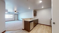 This single-floor unit offers a thoughtfully designed open-concept layout that seamlessly connects the kitchen and living area. The kitchen is equipped with dark espresso cabinetry, granite-style countertops, stainless steel appliances including a refrigerator, range, microwave, and dishwasher, and a peninsula that provides both additional workspace and a natural divider between the kitchen and living areas. Light wood-look flooring runs throughout the kitchen and entryway, while plush carpet covers the spacious living room and bedrooms. The living area is generously proportioned, highlighted by a ceiling fan with light fixture and recessed lighting that keeps the space bright and well-lit. Two bedrooms feature soft carpet flooring and large windows that allow natural light to fill the rooms, with views of the surrounding residential complex. The full bathroom is finished with dark wood cabinetry, a white countertop vanity, a large mirror, and light wood-look flooring that complements the rest of the unit. Dark wood baseboards provide a consistent design accent throughout. An electrical panel is conveniently accessible near the kitchen entry. The overall design is clean, modern, and functional, offering a comfortable and cohesive living environment.