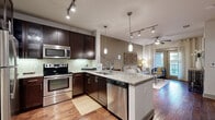 This single-floor residence showcases a thoughtfully designed open-concept layout that seamlessly connects the kitchen, dining, and living areas. The kitchen is a standout feature, equipped with rich dark-espresso cabinetry, stainless steel appliances including a refrigerator, electric range, microwave, and dishwasher, complemented by a light granite peninsula countertop with bar seating. A subway tile backsplash and a combination of track lighting and pendant fixtures illuminate the space with a warm, functional glow. Wood-look flooring flows throughout the main living areas, enhancing the sense of continuity.

The living room is bathed in natural light from floor-to-ceiling glass doors that open to an outdoor area, accented by a ceiling fan and neutral warm-toned walls. The bedroom features plush carpeting, a large window allowing ample natural light, and a bold accent wall, accompanied by a spacious walk-in closet with built-in shelving and hanging rods. The bathroom offers large-format tile flooring, a granite-topped dark vanity with an oversized mirror, and a shower-tub combination, with direct access to the bedroom for added convenience.