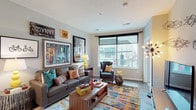 Located on North High Street in Columbus, Ohio, this contemporary single-floor residence offers a vibrant urban living experience in the heart of the city. The open-concept living area is anchored by large windows that frame views of the surrounding cityscape, flooding the space with natural light. Durable hardwood-style flooring runs throughout the main living areas, lending a clean and modern aesthetic.

The kitchen is well-equipped with stainless steel appliances, white shaker-style cabinetry, a gray tile backsplash, and a granite-topped island with an undermount sink — ideal for both cooking and casual dining. Pendant lighting overhead adds a refined finishing touch.

The bedroom is a standout feature, boasting expansive floor-to-ceiling windows that offer sweeping street-level views of North High Street. Soft carpeting, a dedicated workspace, and a spacious sliding-door closet make the room both comfortable and functional.

Two bathrooms provide practical convenience — one with a walk-in shower and hardwood-style flooring, and another with a light, neutral palette and vanity storage. A dedicated utility area with a stacked washer and dryer, water heater, and HVAC equipment rounds out the space, adding everyday practicality to this stylish urban residence.