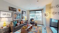 Located on North High Street in Columbus, Ohio, this contemporary single-floor residence offers a vibrant urban living experience in the heart of the city. The open-concept living area is anchored by large windows that frame views of the surrounding cityscape, flooding the space with natural light. Durable hardwood-style flooring runs throughout the main living areas, lending a clean and modern aesthetic.

The kitchen is well-equipped with stainless steel appliances, white shaker-style cabinetry, a gray tile backsplash, and a granite-topped island with an undermount sink — ideal for both cooking and casual dining. Pendant lighting overhead adds a refined finishing touch.

The bedroom is a standout feature, boasting expansive floor-to-ceiling windows that offer sweeping street-level views of North High Street. Soft carpeting, a dedicated workspace, and a spacious sliding-door closet make the room both comfortable and functional.

Two bathrooms provide practical convenience — one with a walk-in shower and hardwood-style flooring, and another with a light, neutral palette and vanity storage. A dedicated utility area with a stacked washer and dryer, water heater, and HVAC equipment rounds out the space, adding everyday practicality to this stylish urban residence.