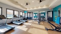 Located at 3 Vantage Way in Greenville, SC, this fitness center offers a comprehensive exercise facility designed to support a wide range of workout routines. The space features a bold and energizing design, with striking teal accent walls contrasted against neutral gray tones, creating a motivating atmosphere for exercise.

The room is filled with natural light streaming through multiple large windows fitted with roller shades, offering views of the surrounding outdoor areas. Recessed lighting and dual ceiling fans ensure the space remains well-lit and comfortable throughout the day. A wall-mounted flat-screen TV is positioned for easy viewing during cardio sessions.

The fitness floor is equipped with a strong lineup of cardio machines, including multiple treadmills, stationary bikes, an elliptical, a rowing machine, and a stair climber. A dedicated strength training area features a multi-station cable machine, an adjustable workout bench, and a full rack of dumbbells in varying weights. Medicine balls and stability balls round out the functional training options.

Large wall mirrors expand the sense of space and allow users to monitor their form during workouts. Durable, cushioned flooring provides comfort and safety throughout the exercise area. The layout is thoughtfully organized to allow ample open floor space, supporting both equipment-based and free-form training with ease.