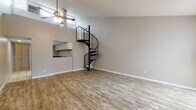 Located in North Haven, Connecticut, this two-floor residence with loft offers a thoughtfully designed layout that balances open living with defined spaces. The main level welcomes you into a spacious living area finished with warm hardwood-style flooring and neutral gray walls that create a clean, modern backdrop. A striking black spiral staircase serves as both a functional and architectural centerpiece, leading up to the loft level above. High transom windows allow natural light to filter in, while a ceiling fan adds comfort overhead. A pass-through opening connects the living area to the kitchen, which is equipped with white cabinetry, dark countertops, a tile floor, and a full appliance suite including an electric range. The bathroom on the main level features a full tub-shower combination accented by bold, dark slate-style wall tile and a classic white vanity. The upper loft level offers a versatile open space with plush carpeting, vaulted ceilings that amplify the sense of height, and access to natural light through vertical-blind-covered windows. A ceiling fan and open railing overlooking the lower level complete this flexible upper retreat, ideal for use as a sleeping area, home office, or lounge.