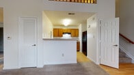 Located at 9901 Gable Ridge Terrace in Rockville, Maryland, this two-floor home offers a well-designed layout with standout architectural details throughout. The main living area impresses with soaring vaulted ceilings and a large arched window that floods the room with natural light. A fireplace serves as a central focal point, complemented by neutral carpet flooring and a secondary window with an exterior door, enhancing the open and airy ambiance. The entry level also features hardwood-style flooring in the foyer, which transitions seamlessly into the kitchen area. The kitchen is equipped with warm oak cabinetry, light stone-finish countertops, a gas range with an overhead exhaust hood, and a black refrigerator, all arranged around a convenient breakfast bar peninsula. A full bathroom on this level includes a wood-toned vanity, large mirror, and clean white fixtures. Upstairs, a carpeted landing with a classic wood banister overlooks the main living area below. The upper level hosts well-proportioned bedrooms with plush carpet, ample closet space including mirrored sliding-door closets, and access to an additional bathroom. The overall design balances comfort and functionality throughout both floors.