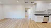 This thoughtfully designed single-floor unit presents a clean, contemporary aesthetic throughout, unified by light wood-style flooring and crisp white walls. The open-concept living and dining area offers a generous, airy feel, with recessed lighting and smooth white ceilings creating a bright, welcoming atmosphere.

The kitchen is a standout feature, outfitted with white shaker-style cabinetry, gray stone countertops, and a full suite of stainless steel appliances including a gas range, microwave, dishwasher, and sink. Ample upper and lower cabinet storage ensures practical functionality alongside a polished appearance.

Multiple bedrooms provide comfortable, well-proportioned spaces, each illuminated by natural light through windows that frame views of mature palm trees and surrounding greenery — lending a distinctly Southern California ambiance. The rooms are finished with the same warm flooring and neutral walls, offering a versatile canvas for any layout.

Two full bathrooms serve the unit, each featuring a tub-and-shower combination enclosed by sliding glass doors, complemented by white cabinetry with matching gray countertops. Recessed lighting and clean finishes complete the bathrooms' modern look.

The unit also includes a dedicated electrical panel, HVAC vents throughout, and a cohesive design language that makes this a move-in ready space with contemporary appeal.