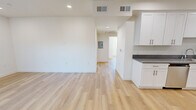 This thoughtfully designed single-floor unit presents a clean, contemporary aesthetic throughout, unified by light wood-style flooring and crisp white walls. The open-concept living and dining area offers a generous, airy feel, with recessed lighting and smooth white ceilings creating a bright, welcoming atmosphere.

The kitchen is a standout feature, outfitted with white shaker-style cabinetry, gray stone countertops, and a full suite of stainless steel appliances including a gas range, microwave, dishwasher, and sink. Ample upper and lower cabinet storage ensures practical functionality alongside a polished appearance.

Multiple bedrooms provide comfortable, well-proportioned spaces, each illuminated by natural light through windows that frame views of mature palm trees and surrounding greenery — lending a distinctly Southern California ambiance. The rooms are finished with the same warm flooring and neutral walls, offering a versatile canvas for any layout.

Two full bathrooms serve the unit, each featuring a tub-and-shower combination enclosed by sliding glass doors, complemented by white cabinetry with matching gray countertops. Recessed lighting and clean finishes complete the bathrooms' modern look.

The unit also includes a dedicated electrical panel, HVAC vents throughout, and a cohesive design language that makes this a move-in ready space with contemporary appeal.