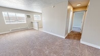 Located at 4515 Shepard Rd NE in Albuquerque, New Mexico, this one-bedroom, one-bathroom unit offers an efficiently organized single-floor layout. The living area features neutral-toned carpet, a textured ceiling, and windows fitted with an in-wall air conditioning unit, allowing for natural light while maintaining climate control. A baseboard heating system runs along the walls, providing supplemental warmth. A compact kitchen peninsula separates the living space from the kitchen, which is finished with light wood-look flooring, white cabinetry with modern bar-pull hardware, a stainless steel sink, and a black electric range beneath a ventilation hood.

A hallway connects the main living area to the bedroom and bathroom. The bedroom is a comfortable size, featuring plush carpet, a sliding glass door that opens to a private balcony with exterior views, and a closet with bi-fold doors offering built-in hanging storage. A wall sconce provides additional lighting. The bathroom includes wood-look flooring, a white vanity, chrome fixtures, and a shower/tub combination, maintaining a clean and functional aesthetic throughout.