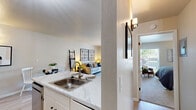 This single-floor unit offers a thoughtfully designed layout encompassing a combined kitchen and living room, one bedroom, and a closet. The open-concept kitchen and living area serves as the heart of the unit, where light wood-style flooring flows throughout. The kitchen is equipped with stainless steel appliances — including a refrigerator, range, and over-the-range microwave — complemented by white cabinetry with matte black hardware and a striking marble-style countertop. A wall sconce adds warm accent lighting to the dining area nearby. The living room is bright and welcoming, featuring a sliding glass door that opens to a private balcony with outdoor views, allowing natural light to fill the space. The bedroom features plush carpeting, neutral-toned walls, and a window with balcony access, creating a calm and restful retreat. The closet provides practical storage. Throughout the unit, a cohesive neutral palette, clean lines, and modern fixtures contribute to a contemporary and comfortable ambiance. The efficient use of space makes this unit an ideal option for those seeking a functional, modern living environment.