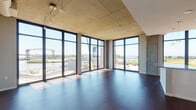 Located along the Cuyahoga River in Cleveland's Flats neighborhood, this contemporary unit at 1055 Old River Rd offers an impressive blend of industrial-modern architecture and refined finishes. The open-concept living area is defined by dramatic floor-to-ceiling windows that wrap around the corner, flooding the space with natural light and framing panoramic views of the river and Cleveland's historic lift bridge. Exposed concrete ceilings and rich dark hardwood flooring throughout create a striking contrast that reinforces the space's urban character.

The kitchen is thoughtfully appointed with high-gloss white cabinetry, granite countertops, a center island with breakfast bar, and a full suite of stainless steel appliances, including a refrigerator, range, microwave, and dishwasher. The sleeping areas feature plush carpeting and exposed concrete ceilings, with the primary bedroom offering direct access to a private balcony overlooking the river. Two bathrooms are finished with neutral tile, granite-topped vanities, and modern white cabinetry. A second bedroom provides a quiet, well-proportioned retreat. Throughout the unit, the design balances raw architectural elements with clean, contemporary details, resulting in a distinctive and light-filled riverfront residence.