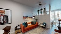 Located at 2183 E Apache Blvd in Tempe, Arizona, this single-floor unit presents a thoughtfully designed interior that balances modern functionality with bold, eclectic style. Light wood-tone flooring runs throughout, creating a cohesive foundation that connects each area of the space seamlessly.

The living area serves as the heart of the unit, anchored by a striking orange tufted sofa, layered with teal and charcoal accent pillows. A large abstract canvas adds a colorful focal point to the neutral walls, while an arc floor lamp and hanging trailing plants introduce organic texture overhead. A ceiling fan provides both style and practicality. The living area opens toward a dedicated dining nook, furnished with a round white table and modern chairs, accented by eclectic wall art.

The kitchen features two-tone cabinetry — warm wood lower cabinets paired with crisp white uppers — complemented by stone-look countertops and stainless steel appliances, including a range, microwave, and refrigerator. Light wood flooring continues here, reinforcing the clean, contemporary aesthetic.

The bedroom is a calm retreat, highlighted by a large window that invites natural light, dressed with patterned curtains and blinds. A bold floral canvas adds a vibrant accent above the bed.

The bathroom offers warm wood cabinetry, a shower with a decorative curtain, and clean white fixtures, maintaining the unit's cohesive modern character throughout.