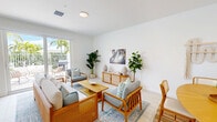 Located at 3640 Blue Fin Way in Fort Myers, Florida, this two-story, two-bedroom, two-bathroom home offers a bright and airy coastal aesthetic throughout. The main floor hosts an open-concept living, dining, and kitchen area finished with light tile flooring. The kitchen features light wood cabinetry, a white quartz peninsula with bar seating, stainless steel appliances, and recessed lighting. The adjacent living room is filled with natural light and opens via sliding glass doors to a private balcony with views of swaying palm trees. A coastal-inspired dining nook with warm wood furnishings and artisan wall décor completes the main level. Upstairs, warm hardwood-style flooring flows through the hallway and into both bedrooms. The primary bedroom is a generous retreat featuring a walk-in closet with full hanging storage. The second bedroom offers dual windows that invite ample natural light and outdoor views. Both bathrooms are finished with neutral tile, wood-toned vanities, white quartz countertops, and frameless glass-enclosed walk-in showers. The home's clean white walls, consistent warm-toned wood accents, and coastal décor create a cohesive, serene atmosphere throughout.