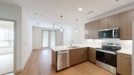 Located at 1455 Moonrise Avenue in Carrollton, TX, this two-bedroom, two-bathroom residence offers a well-designed single-floor layout with a clean, modern aesthetic throughout. The open-concept kitchen and living area serves as the heart of the home, featuring warm wood-grain cabinetry, crisp white quartz countertops, a full suite of stainless steel appliances including a refrigerator, electric range, built-in microwave, and dishwasher, and stylish pendant lighting over the peninsula. Light wood-style flooring extends through the main living areas, complementing the neutral color palette and recessed lighting. The living room benefits from natural light through full-length glass doors, with a ceiling fan adding comfort. The primary bedroom offers wood-style flooring, a ceiling fan, and access to a well-organized walk-in closet with multi-level shelving and hanging rods. The second bedroom features plush carpeting and a bright window. Both bathrooms are finished with wood-toned vanities, white quartz counters, and tiled tub-shower combinations, with one bathroom also including built-in open shelving for additional storage. The overall ambiance is bright, contemporary, and functional.