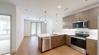 Located at 1455 Moonrise Avenue in Carrollton, TX, this two-bedroom, two-bathroom residence offers a well-designed single-floor layout with a clean, modern aesthetic throughout. The open-concept kitchen and living area serves as the heart of the home, featuring warm wood-grain cabinetry, crisp white quartz countertops, a full suite of stainless steel appliances including a refrigerator, electric range, built-in microwave, and dishwasher, and stylish pendant lighting over the peninsula. Light wood-style flooring extends through the main living areas, complementing the neutral color palette and recessed lighting. The living room benefits from natural light through full-length glass doors, with a ceiling fan adding comfort. The primary bedroom offers wood-style flooring, a ceiling fan, and access to a well-organized walk-in closet with multi-level shelving and hanging rods. The second bedroom features plush carpeting and a bright window. Both bathrooms are finished with wood-toned vanities, white quartz counters, and tiled tub-shower combinations, with one bathroom also including built-in open shelving for additional storage. The overall ambiance is bright, contemporary, and functional.