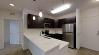 This single-floor space showcases a thoughtfully designed, contemporary kitchen as its centerpiece. Rich, dark espresso-toned cabinetry lines the walls, providing ample storage while creating a striking contrast against the bright white quartz countertops and peninsula. The peninsula offers generous workspace and serves as a natural divider between the kitchen and the adjacent living area, making it ideal for both meal preparation and casual dining.

The kitchen is outfitted with a full suite of stainless steel appliances, including a refrigerator, an electric range, and a built-in microwave, all seamlessly integrated into the cabinetry for a cohesive, polished look. A deep undermount sink is centrally positioned within the peninsula for added convenience.

Overhead, elegant pendant lights hang above the peninsula, casting warm, focused illumination that complements the recessed and flush-mount lighting throughout the space. The light-toned flooring adds brightness and continuity, enhancing the overall sense of openness. Clean white walls and a neutral color palette create a modern, airy ambiance throughout, making the space feel welcoming and versatile. The layout is efficient and well-organized, reflecting a practical yet stylish approach to contemporary interior design.