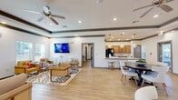 Located at 1880 Pat Thomas Pkwy in Quincy, Florida, this single-story community space offers a thoughtfully designed open-concept floor plan that flows seamlessly from one area to the next. The interior is characterized by warm light wood flooring throughout, crisp white walls, and distinctive tray ceilings accented with dark wood crown molding detail, lending a refined yet welcoming ambiance.

The welcoming reception lobby features structural columns, large glass entry doors, and an abundance of natural light from surrounding windows. A decorative round glass table serves as a central focal point, complemented by framed service windows along the wall.

The expansive lounge area provides generous seating with multiple coordinated armchairs and sofas arranged over geometric patterned area rugs. A wall-mounted flat-screen TV, ceiling fan, and recessed lighting enhance the comfortable, community-oriented atmosphere. Large windows allow natural light to fill the room.

The kitchen is fully equipped with warm honey-toned wood cabinetry, marble-look quartz countertops, a black French door refrigerator, and a kitchen island with bar seating. Elegant globe pendant lights hang above, while recessed lighting ensures the space is bright and functional. A dining area with a round table and modern chairs sits adjacent, completing this versatile community gathering space.