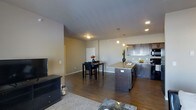 This single-floor residence showcases an open-concept layout that integrates the living, dining, and kitchen areas into one cohesive space. The kitchen is a standout feature, equipped with dark espresso-toned cabinetry that extends to the upper walls, providing ample storage. A central island with a granite-style countertop serves as both a functional workspace and a visual anchor for the space, complemented by modern pendant lighting that hangs above it. Additional recessed lighting throughout ensures the area is well-lit. The kitchen also includes stainless steel appliances and a sink positioned along the back counter, offering a practical and stylish setup.

Rich, dark hardwood flooring spans the living and dining areas, adding warmth and continuity to the open floor plan. The dining area comfortably accommodates a table and chairs, making it ideal for everyday meals or entertaining. Adjacent to the dining space, the living area features a plush area rug and media console, creating a relaxed and inviting atmosphere. Neutral-toned walls throughout the space provide a clean, versatile backdrop that complements the darker furnishings and finishes.