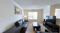 This single-floor residence presents a well-organized and functional layout designed for comfortable everyday living. The living room is finished with wall-to-wall carpeting and features crown molding that adds a refined architectural touch. A large window fills the space with natural light, creating a bright and welcoming atmosphere. The textured ceiling and neutral wall tones contribute to a clean, understated aesthetic throughout.

The kitchen is outfitted with white cabinetry that extends to the upper walls, providing ample storage space. A peninsula with an integrated sink serves as a convenient breakfast bar, seamlessly connecting the kitchen to the adjacent living areas. White appliances, including a refrigerator, microwave, and range, are neatly integrated into the cabinetry, maintaining a cohesive and tidy appearance. The kitchen floor transitions to tile, offering a practical and easy-to-clean surface.

A hallway visible from the kitchen leads to the bedroom, which features carpeted flooring consistent with the rest of the unit. The overall design of the space prioritizes functionality and comfort, with a neutral color palette that lends itself well to a variety of interior styles. The thoughtful flow between rooms makes this a practical and livable space.