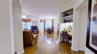 This single-story, 3-bedroom, 2-bathroom residence is thoughtfully laid out to maximize its compact footprint. The living room serves as a welcoming centerpiece, featuring gleaming hardwood floors, crown molding, a ceiling fan, and multiple windows dressed with layered blinds and fabric valances that allow abundant natural light. A bold accent wall in warm gold tones adds character, complemented by framed artwork and a blue sofa with coordinating décor.

The adjoining dining area flows naturally from the living space, featuring a round table beneath a pendant light and windows overlooking the exterior. The kitchen offers light wood cabinetry, a stainless steel refrigerator, ample counter space, and hardwood-style flooring. A distinctive built-in desk nook with open shelving provides a functional workspace just off the main living area.

The primary bedroom includes carpeted flooring, a ceiling fan, and a walk-in closet with wire shelving. Additional bedrooms feature accent walls and warm lighting. Both bathrooms are functional, with one including a tub-shower combination and warm wood vanity cabinetry. Two hallways connect the private and shared spaces efficiently throughout the home.