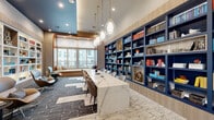 Located at 275 Pine Terrace Dr in Conroe, TX, this thoughtfully designed office space blends functionality with sophisticated style. The single-floor layout offers a well-appointed workspace anchored by a striking marble-topped communal work table, surrounded by contemporary upholstered chairs — ideal for focused work or collaborative sessions.

A dramatic floor-to-ceiling built-in bookcase serves as the centerpiece of the room, finished in deep navy blue and warm wood tones and filled with curated books and decorative objects. A complementary white built-in shelving unit along another wall adds brightness and additional display space, both illuminated with integrated lighting.

Overhead, a cluster of elegant glass teardrop pendant lights suspended by brass fixtures draws the eye upward, enhancing the room's refined ambiance. The ceiling features a bold navy blue tray detail that adds architectural depth and contrast.

Natural light pours in through large windows fitted with sheer roller shades, accompanied by a cushioned window seat — a comfortable nook for reading or relaxing. The patterned area rug in charcoal and white tones adds texture underfoot, while modern swivel lounge chairs and a glass-topped side table complete a stylish reading corner. Glass partition walls provide visual connectivity to adjacent spaces while maintaining a sense of privacy.