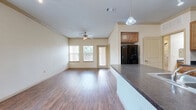 Located in Waller, TX, this single-story, one-bedroom, one-bathroom home offers a well-designed layout that maximizes comfort and functionality. The open-concept living area features warm wood-look flooring, crown molding, and a ceiling fan with light fixture, creating a bright and inviting atmosphere. Multiple windows allow natural light to fill the space, offering pleasant outdoor views and a connection to the surrounding greenery.

The kitchen is well-appointed with warm wood cabinetry, dark granite-style countertops, black appliances including a range, microwave, and refrigerator, and a peninsula that seamlessly connects to the living area. Track lighting and a pendant light add purposeful illumination throughout.

The bedroom is carpeted for comfort, featuring vaulted ceilings, dual windows with blinds, and a ceiling fan. A spacious walk-in closet provides ample storage with built-in shelving, hanging rods, and a dedicated shelf unit for organization.

The bathroom is finished with clean white tile flooring, a vanity with dark countertops and wood cabinetry, a large mirror, and a separate soaking tub and shower area accessed through a windowed alcove. A built-in shelving nook and desk area in an additional room add further versatility to this thoughtfully designed home.