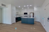 This 620-square-foot, one-bedroom, one-bathroom apartment in Washington, Utah, features a clean, modern design with consistent light wood-look flooring throughout the main living areas and a bright, neutral color palette. The open-concept kitchen and living room form the heart of the unit, showcasing a striking two-tone kitchen with deep teal lower cabinetry, white upper cabinets, and crisp white quartz countertops. A central island adds workspace and storage, while stainless steel appliances — including a refrigerator, range, microwave, and dishwasher — complete the well-appointed kitchen. Recessed lighting illuminates the space overhead. The living area offers access to an outdoor balcony through a glass door, allowing generous natural light to fill the room. The 120-square-foot bedroom features plush carpet flooring and a large window with outdoor views. The full bathroom is elegantly finished with a dark teal vanity, dual sinks, a large mirror, and wood-look flooring, complemented by an adjacent closet with barn-style doors. A hallway connects all rooms efficiently. The unit's crisp white walls, modern hardware, and cohesive design elements create a polished, contemporary living environment.