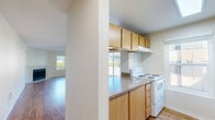 Located at 12316 28th Ave NE in Seattle, WA, this two-bedroom, two-bathroom residence offers a practical and comfortable single-level layout. The combined kitchen and living room serves as the heart of the home, featuring warm hardwood-style flooring, a ceiling fan, and a fireplace framed by a large window that fills the space with natural light and views of the surrounding greenery. The kitchen is efficiently designed in a galley style, with light wood cabinetry, granite-style countertops, a white electric range, and a dishwasher. A peninsula counter connects the kitchen to the living area, creating an open, cohesive flow. Both bedrooms are carpeted and well-proportioned, with the primary bedroom offering generous room for furnishings. Each bedroom benefits from natural light via windows, and both include dedicated closets with sliding wood-panel doors. The two bathrooms are clean and functional, each featuring a full bathtub and shower combination with brushed nickel fixtures and hardwood-style flooring. Additional storage is available through two closets throughout the unit. The overall ambiance is bright, neutral, and move-in ready, making it a well-rounded home in a convenient Seattle neighborhood.