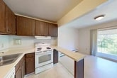 Located at 311 W Seneca St in Manlius, NY, this two-bedroom, one-bathroom single-floor unit offers a functional and well-organized layout. The kitchen features dark wood cabinetry, light countertops, a coil-burner electric range, a refrigerator, and a stainless steel sink. A peninsula counter separates the kitchen from the adjacent living area, creating an open, connected feel. Light tile flooring runs throughout the kitchen, while baseboard heating is present throughout the unit. The living room is generously sized, finished with neutral carpet and a pair of windows that let in natural light and views of surrounding greenery. Two hallways connect the main living spaces to the private quarters. The primary bedroom is a well-proportioned room featuring soft carpet, a window with natural light, and a full wall of built-in bi-fold closets with gold hardware, providing excellent storage. The second bedroom is similarly carpeted and bright, with a window and baseboard heating. The full bathroom includes a single-sink vanity with a wood cabinet base, a large mirror, tile flooring, and a full tub-shower combination with white tile surround. The overall aesthetic is clean and neutral, making this a straightforward and practical living space.