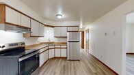 Located at 1110 S Wells St in Lake Geneva, Wisconsin, this 2-bedroom, 1-bathroom unit offers a functional and well-appointed single-floor layout. The open-concept kitchen and living area serves as the heart of the home, featuring light wood-style flooring throughout, warm wood trim accents, and a ceiling fan that adds comfort and airflow. The kitchen is well-equipped with stainless steel appliances including an electric range and full-size refrigerator, complemented by white cabinetry with wood trim detailing, a butcher block-style countertop, a built-in range hood, and a corner sink with pendant lighting above. The living room benefits from natural light through dual windows with wood-framed trim and includes a baseboard heating unit. The primary bedroom offers generous closet space with two sets of bifold doors and direct access to a private deck through a sliding glass door, bringing in additional natural light and outdoor views. The second bedroom features soft carpeting and warm-toned wood doors. The bathroom includes a full tub and shower combination in a clean, white finish. The overall aesthetic is clean, simple, and move-in ready, ideal for those seeking comfortable living near the amenities of Lake Geneva.