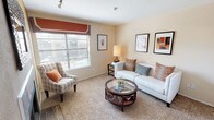 Located at 2101 Pinehurst Ln in Mesquite, TX, this single-floor residence offers a well-organized layout designed for comfortable everyday living. The living room is warm and inviting, finished with plush carpeting, neutral beige walls, and a large window dressed with blinds that allows natural light to fill the space. The kitchen features dark countertops, white cabinetry, black appliances including an electric range and over-the-range microwave, and rich wood-look flooring that extends into the entryway. The primary bedroom is generously sized, highlighted by a bold accent wall and a convenient vanity area with white cabinetry, a large mirror, and track lighting that opens directly into the bathroom. The bathroom is finished with dark wood-look flooring, a dark countertop vanity, and a shower-tub combination. A second bedroom provides a comfortable retreat with carpeted flooring, a window with blinds, and ample wall space. Throughout the residence, warm earth tones, consistent carpeting in the bedrooms, and wood-look hard flooring in wet areas create a cohesive and practical aesthetic. The layout flows efficiently, making the most of the available space across all rooms.