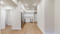 This single-floor unit offers a clean, contemporary design throughout, with warm wood-look flooring and crisp white walls creating a cohesive, bright aesthetic. The kitchen serves as a functional centerpiece, featuring an abundance of white shaker-style cabinetry accented by gold hardware that extends to the ceiling for maximum storage. A full suite of stainless steel appliances includes a refrigerator, range with over-the-range microwave, and dishwasher, all complemented by light countertops and a modern sink fixture. Recessed lighting illuminates the space from above, enhancing the airy feel of the elevated ceiling line in the kitchen area.

The bedrooms are finished with the same warm wood-look flooring and neutral walls, offering versatile, well-proportioned spaces. One bedroom benefits from a window overlooking greenery, bringing in natural light and a connection to the outdoors.

The bathroom is thoughtfully appointed with a frameless glass-enclosed walk-in shower clad in large-format tile, a white vanity with a clean countertop, and distinctive penny tile flooring that adds a refined textural detail. A second bathroom mirrors this design, maintaining consistency throughout the unit. The overall layout, as seen in the 3D overview, is organized and efficiently configured.