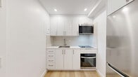 Located at 1240-1250 Rue du Fort in the heart of Montréal, this studio unit offers a thoughtfully designed single-floor layout that maximizes every square foot of its compact footprint. The interior is finished in a clean, modern aesthetic throughout, with crisp white walls, recessed pot lighting, and warm light oak hardwood flooring that runs seamlessly across the living spaces.

The kitchen is efficiently arranged along a single wall, featuring sleek high-gloss white cabinetry — both upper and lower — paired with a white quartz countertop, an undermount stainless steel sink, a black glass induction cooktop, a built-in stainless steel oven, and an over-the-range microwave. The design is both functional and visually polished.

The open living area is bright and versatile, with recessed lighting and a window that provides natural light and a view of the surrounding exterior. A sliding-door closet with built-in rod and shelving offers practical storage within the main living space, alongside baseboard heating for year-round comfort.

The bathroom is finished with large-format ceramic tile from floor to ceiling, and includes a full soaking bathtub, toilet, and vanity with mirror — all rendered in a clean, neutral palette that complements the rest of the unit's modern style.
