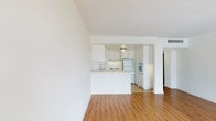 This single-floor residence offers a clean, functional layout with a bright and open feel throughout. The living area is finished with warm wood-style flooring and flows seamlessly into the kitchen via a peninsula-style breakfast bar, creating an open and connected living space. A sliding glass door leads to a generously sized balcony finished with terracotta tile flooring, offering panoramic city views and ample natural light to the main living area.

The kitchen is well-appointed with white cabinetry extending to the ceiling for abundant storage, light-toned countertops, a double sink, electric cooktop, dishwasher, wall oven, and a full-size refrigerator. The tile flooring in the kitchen complements the overall clean, white aesthetic.

The bedrooms are carpeted and comfortably sized, each featuring closet space and access to natural light. The primary bedroom includes a sliding glass door opening to the balcony, further enhancing its airy ambiance with sweeping outdoor views.

The bathroom features a long vanity with a wide mirror, white cabinetry with ample storage, and tile flooring throughout, connecting to a separate water closet for added privacy and convenience.

Throughout the residence, textured ceilings, white walls, and central air conditioning contribute to a bright, well-maintained, and cohesive living environment.