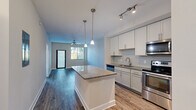 Located in Pembroke Pines, FL, this well-appointed one-bedroom, one-bathroom residence offers a thoughtfully designed layout that maximizes comfort and functionality. The open-concept kitchen and living area serves as the heart of the home, anchored by a central granite-topped island with pendant lighting overhead. The kitchen is outfitted with crisp white shaker-style cabinetry, a subway tile backsplash, granite countertops, and a full suite of stainless steel appliances including a range, microwave, dishwasher, and refrigerator. Track lighting and wood-style flooring complete the modern aesthetic. The living area extends naturally from the kitchen, featuring a ceiling fan and a glass door that opens to an outdoor balcony, filling the space with natural light and views of surrounding greenery. A hallway connects the main living space to two closets, the bathroom, and the bedroom. The bedroom is a comfortable retreat with plush carpeting, a ceiling fan, and a window framing pleasant outdoor views. The bathroom is finished with granite countertops, a framed mirror, gray cabinetry, and a tiled tub-shower combination. Neutral tones and consistent finishes throughout create a cohesive and move-in-ready environment.