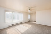 This single-floor unit offers a clean, functional layout designed to maximize comfort and usability. The living area is generously sized, featuring neutral-toned carpet, a ceiling fan with light fixture, and large windows dressed with vertical blinds that allow abundant natural light to fill the space. Baseboard heating units run beneath the windows, providing consistent warmth throughout. The open feel of the room is enhanced by smooth white walls and an unobstructed flow into adjacent areas.

The galley-style kitchen is efficiently arranged, featuring warm honey-toned wood cabinetry lining both walls, dark laminate countertops, and wood-look flooring. White appliances, including a coil-top electric range, refrigerator, and dishwasher, are included. A pass-through view from the kitchen into the living area adds to the sense of openness.

The bedroom is a well-proportioned, carpeted room with a window fitted with horizontal blinds, a baseboard heater, and clean white walls offering a versatile canvas for furnishing. Additional carpeted space visible in the floor plan model suggests further room configurations within the unit.

The bathroom features a full tub-and-shower combination with white subway tile surround, a curtain rod, and wood-look flooring, maintaining the unit's consistent, practical aesthetic throughout.