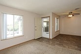 This single-floor unit offers a practical and well-organized layout spread across several functional spaces. The living area is carpeted in a neutral gray tone and benefits from large windows that allow natural light to fill the room, offering views of the surrounding neighborhood. A ceiling fan provides added comfort, while textured ceilings carry throughout the common areas. An entry door with a glass storm door connects the living space to a separate area with wood-look vinyl flooring, providing a natural transition point into the unit.

The kitchen is equipped with warm-toned wooden cabinetry offering generous storage, complemented by light countertops. White appliances include a full-size refrigerator, an electric coil range, and an over-the-range microwave, providing all essential cooking conveniences. Wood-look flooring continues underfoot in this area.

The bedrooms are carpeted and finished in soft neutral tones, with one room featuring a ceiling fan and a window with exterior views. Both rooms provide comfortable proportions suitable for standard furnishings.

The bathroom features wood-look vinyl flooring, a full soaking tub and shower combination, and neutral taupe walls with brushed nickel hardware accents. A dedicated laundry room houses a full-size washer and dryer alongside overhead shelving, rounding out this unit's practical and complete feature set.