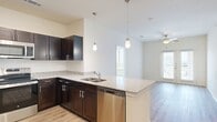 This well-appointed 3-bedroom, 2-bathroom single-floor residence offers a thoughtfully designed open-concept layout that seamlessly connects the kitchen and living areas. The kitchen is a standout feature, showcasing rich dark espresso cabinetry, granite countertops, a large peninsula island with an undermount sink, and a full suite of stainless steel appliances including a refrigerator, range, microwave, and dishwasher. Stylish pendant lighting hangs above the island, adding a modern touch. Light hardwood-style flooring flows throughout the main living areas, complementing the bright, neutral color palette. The living room is bathed in natural light through large windows and French doors, which open to the outdoors, and is finished with a ceiling fan overhead. The bedrooms feature plush carpeting and ceiling fans, with windows that bring in natural light and outdoor views. The primary bedroom includes a walk-in closet with built-in wire shelving for generous storage. Both bathrooms mirror the kitchen's design aesthetic with dark cabinetry, granite countertops, and clean white tile surrounds in the tub and shower areas. A hallway connects the bedrooms and additional closet space rounds out this functional and stylish home.